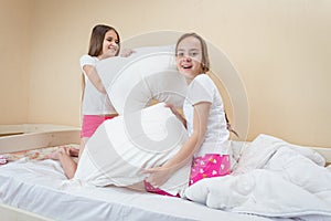 Cheerful teenage girls in pajamas having fun and pillow fight in bedroom