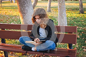 Cheerful teenager girl reading book on the bench at autumn park