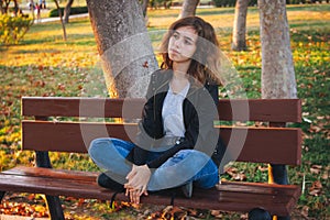 Cheerful teenager girl sitting on the bench at autumn park