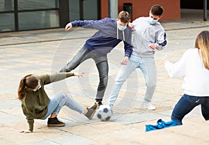 Cheerful teenagers are jogning with ball on street