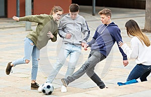 Cheerful teenagers are jogning with ball on street