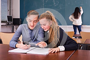 Cheerful teenagers with phone in schoolroom