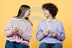 Cheerful teenagers using smartphones isolated on yellow.