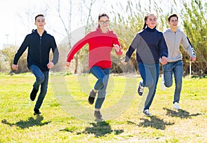 Cheerful teens running on green lawn