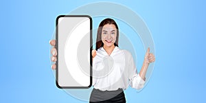 Cheerful thumb up woman showing smartphone with blank screen