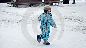 Cheerful toddler boy in snowboots and ski suit happily running on street covered with snow. Cheerful baby, kids playing at winter photo