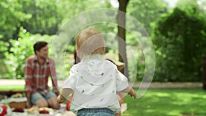 Cheerful toddler running in park. Children having picnic with parents in forest