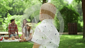 Cheerful toddler running in park. Children having picnic with parents in forest