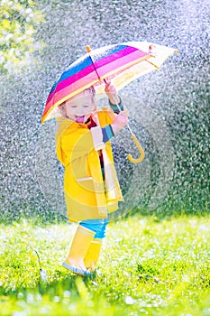 Cheerful toddler with umbrella playing in the rain