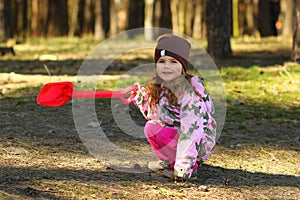 Cheerful todler girl showing the way in the forest with a red shovel