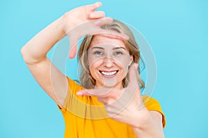 Cheerful toothily smiling woman making frame gesture in studio