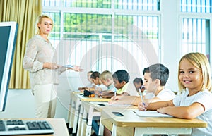 Cheerful towheaded preteen schoolgirl looking at camera in class