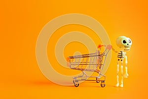 Cheerful toy skeleton with shopping cart on orange background with copy space