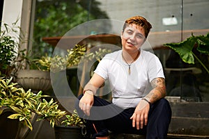 Cheerful transgender person in casual wear works on laptop at co-working space. Inclusive workspace ambience with plants