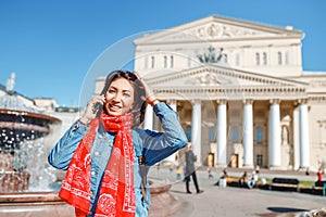 Cheerful traveler girl talking by phone at the Bolshoi Theatre in the background