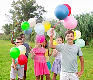 Cheerful tween boy with balloons spending time with friends in park