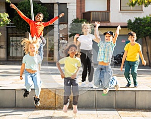 Cheerful tween girls and boys jumping on summer city street