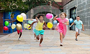 Cheerful tweenagers with balloons in hands running on city street