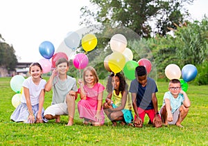 Cheerful tweenagers with colored balloons posing together in summer park