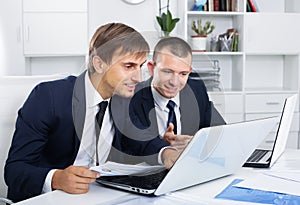 cheerful two men coworkers working on computers in firm office