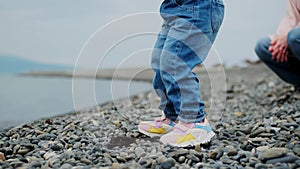 Cheerful unrecognizable child on seashore or ocean on beach throws stones into pond. Colorful colored sneakers of small