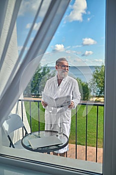 Cheerful vacationer with the open newspaper in his hands looking away