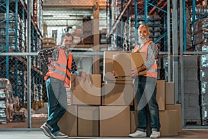 cheerful warehouse workers standing with boxes and smiling