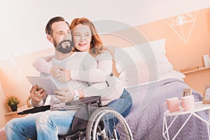 Cheerful wheelchaired man using a tablet with his wife