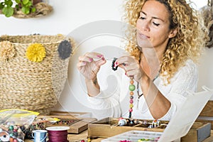 Cheerful woman adult at home doing necklace jewels with colorful beads - home work and alternative job oportunity for modern and