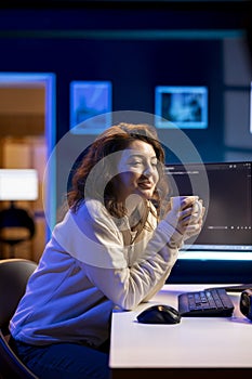 Cheerful woman in apartment enjoying hot beverage, using computer