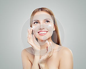 Cheerful woman applying facial cosmetic cream and smiling on white background. Beautiful female model portrait