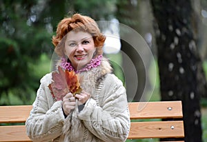 The cheerful woman of average years holds autumn maple leaves in hand