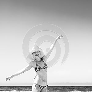 Cheerful woman in beachwear and straw hat on the seashore