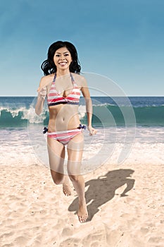 Cheerful woman in bikini jogging on beach
