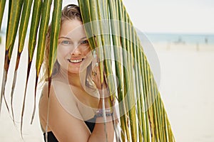 Cheerful woman in black swimsuit standing near palm tree