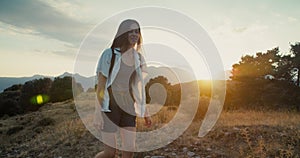 Cheerful woman climbing up the mountain on summer journey at sunset