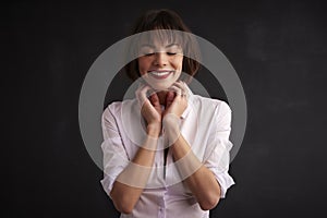 Cheerful woman with closed eyes standing at dark background photo