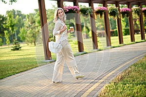 Cheerful woman with coffee walking in park