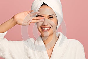 Cheerful woman covering eye with two fingers in studio