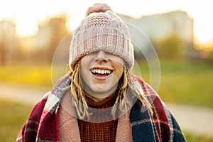 Cheerful woman covering eyes with knit hat while standing outdoors