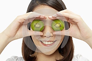 Cheerful woman covering her eyes with a kiwi