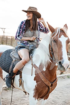 Cheerful woman cowgirl sitting and riding horse in village