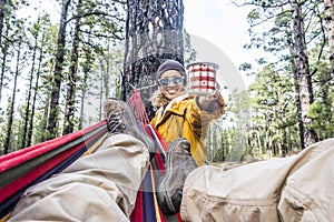 Cheerful woman with cup of coffe enjoy the nature relax outdoor leisure activity with man laying on the hammock - happy people in