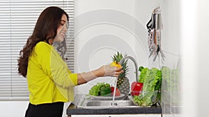 Cheerful woman dancing while washing vegetables in the sink in the kitchen at home