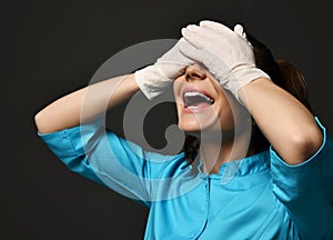 Cheerful woman doctor gynecologist reproductologist in white latex gloves and blue uniform standing and covering eyes