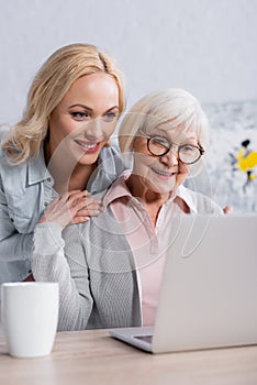 Cheerful woman embracing senior mother near