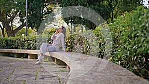 Cheerful woman enjoy phone conversation sitting on park bench at green foliage photo