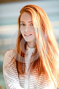 Cheerful woman with green eyes and red hair in white striped blouse l