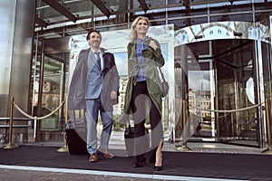Cheerful woman and a happy man leaving a hotel with their luggage