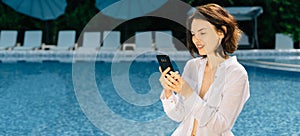 cheerful woman having a rest near swimming pool with a mobile phone leads a live broadcast or has a video call with